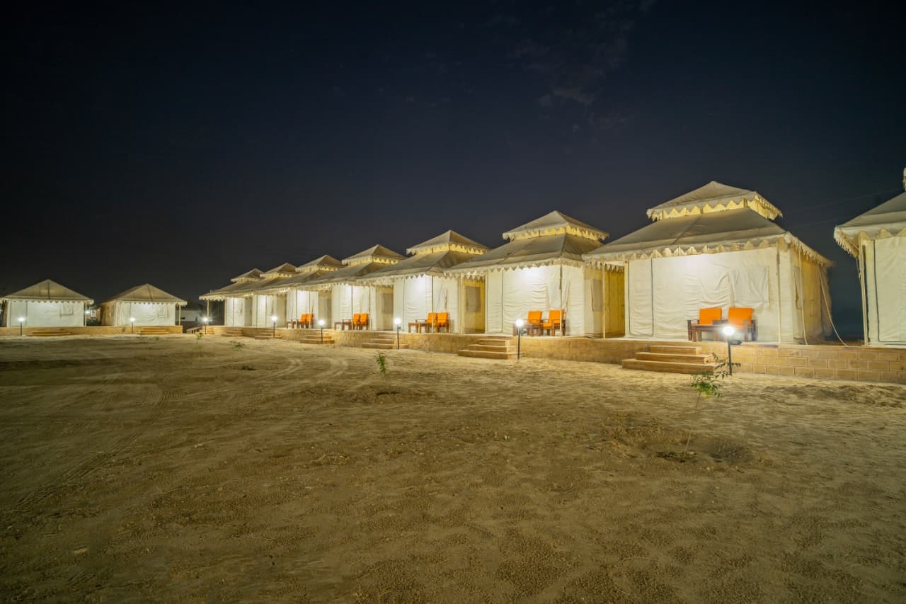 Wide night view of the Desert Overnight Camp tent row across the sand