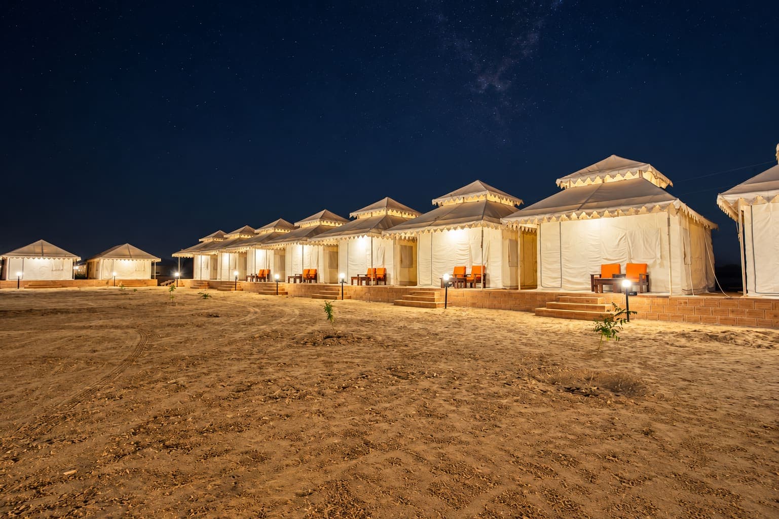 Wide night view of the Desert Overnight Camp tent row across the sand