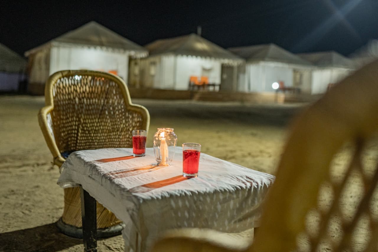Welcome drinks and a candle lantern on a dining table set outdoors on the dunes