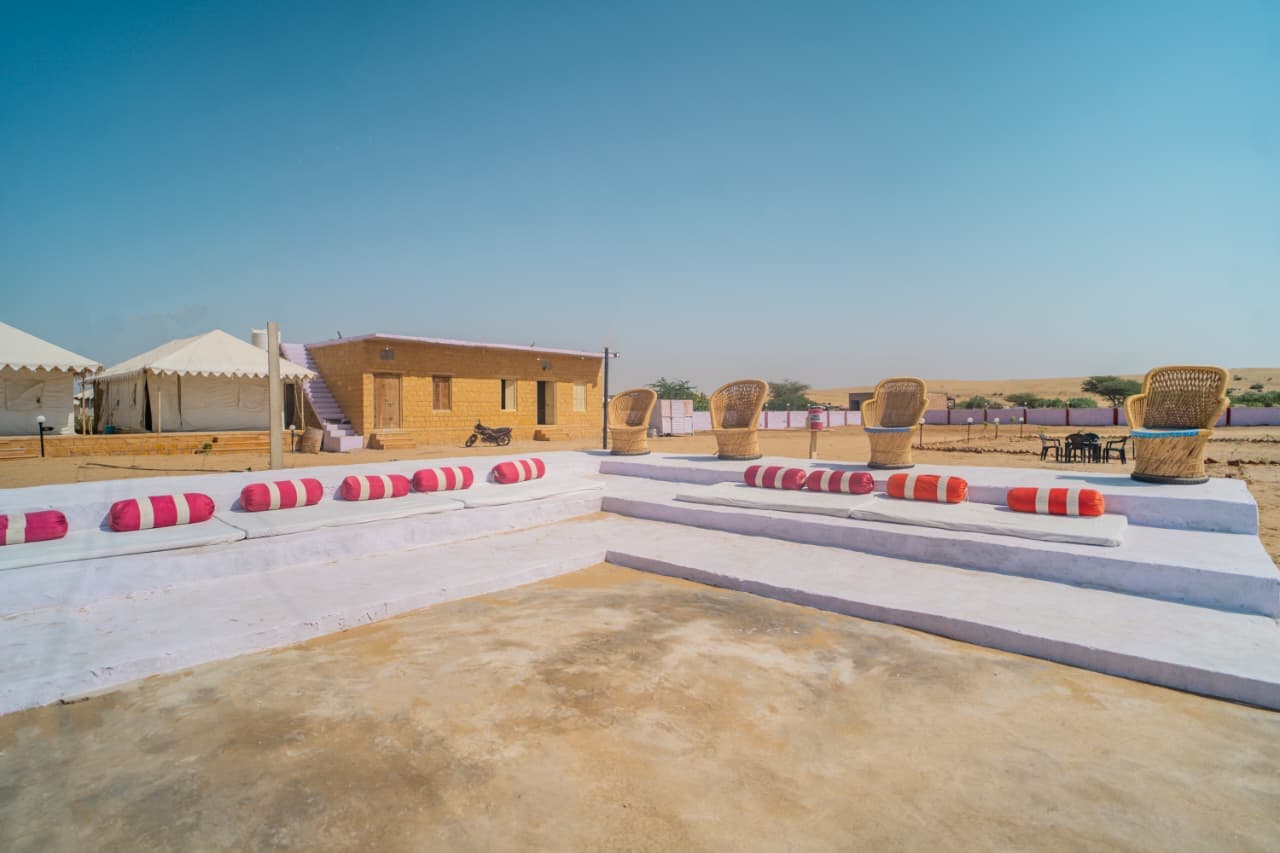 Open-air bolster seating and cane chairs facing the Thar Desert at the camp