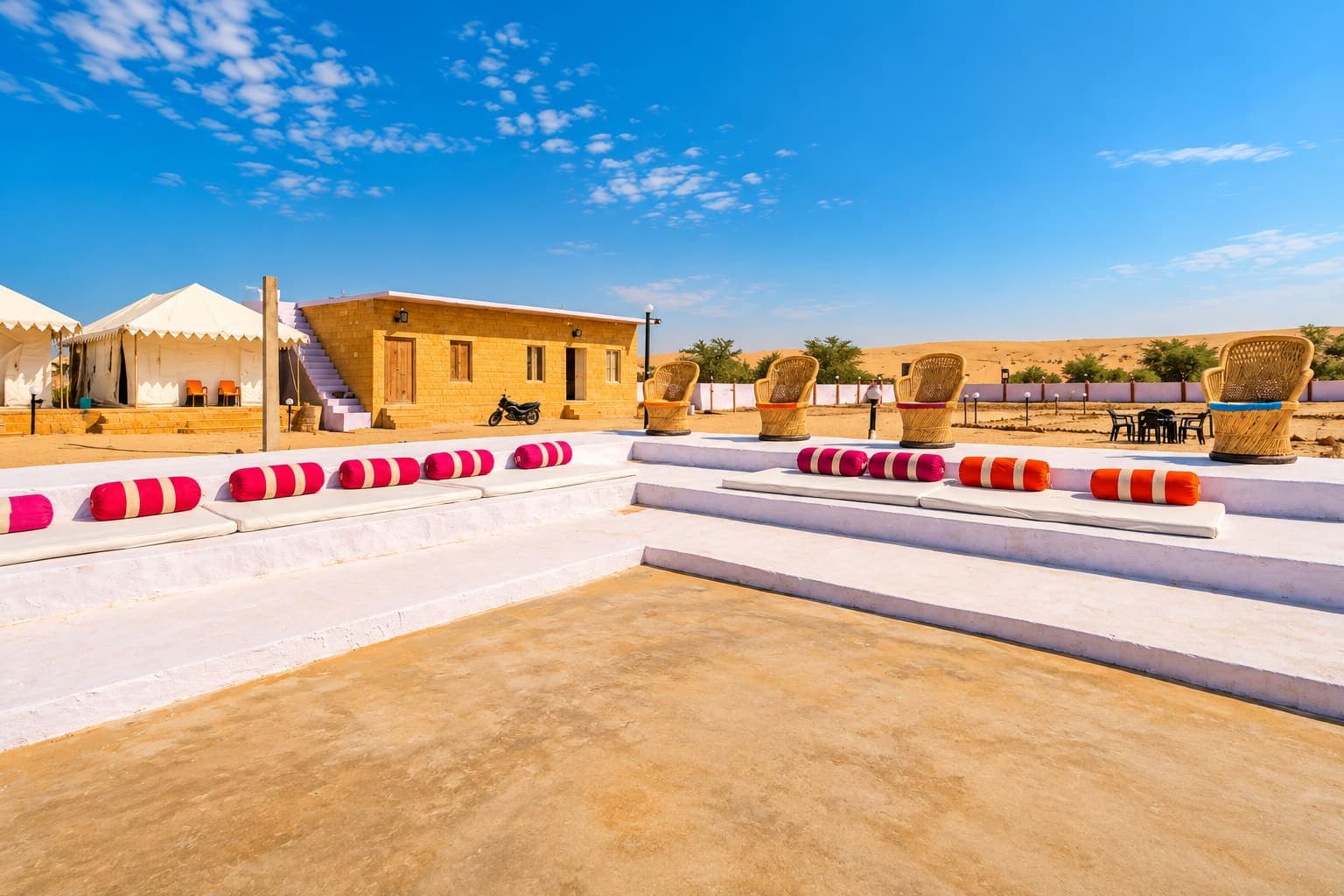 Open-air bolster seating and cane chairs facing the Thar Desert at the camp