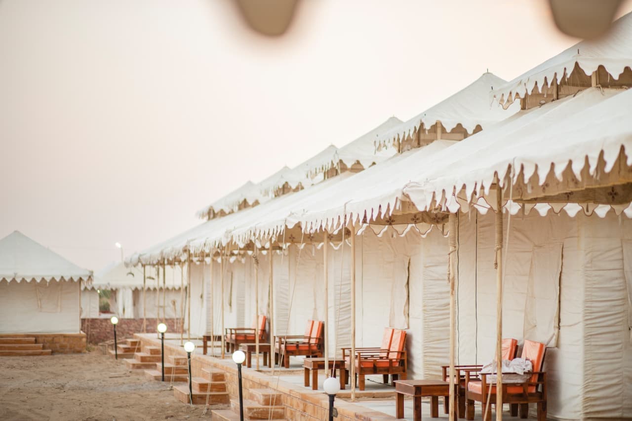 Swiss tents with cushioned sit-outs under a pink dusk sky at our Jaisalmer desert camp